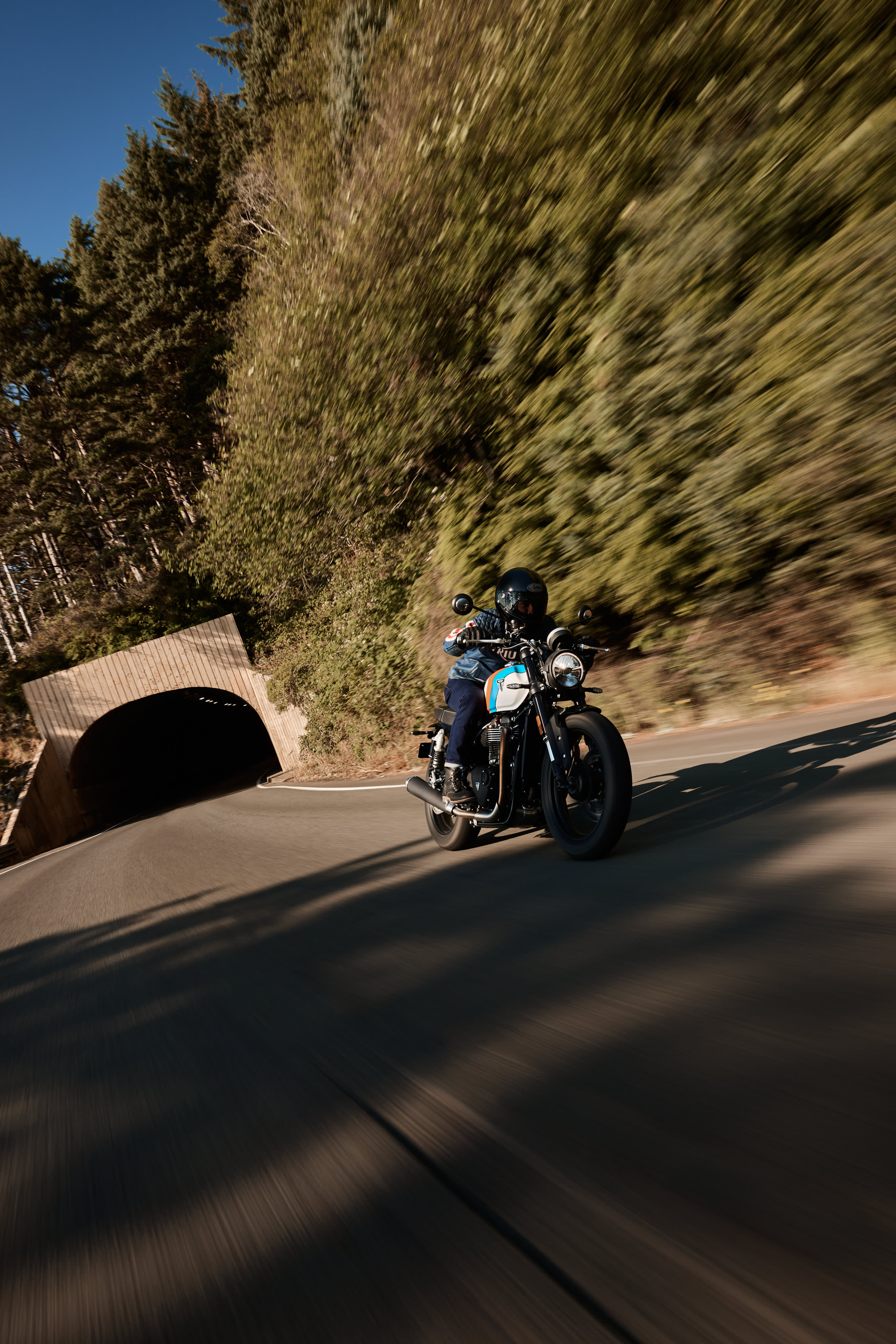 Angled front view action shot of a rider on Triumph Speed Twin 900 in Pure White / Maui Blue / Tangerine Orange