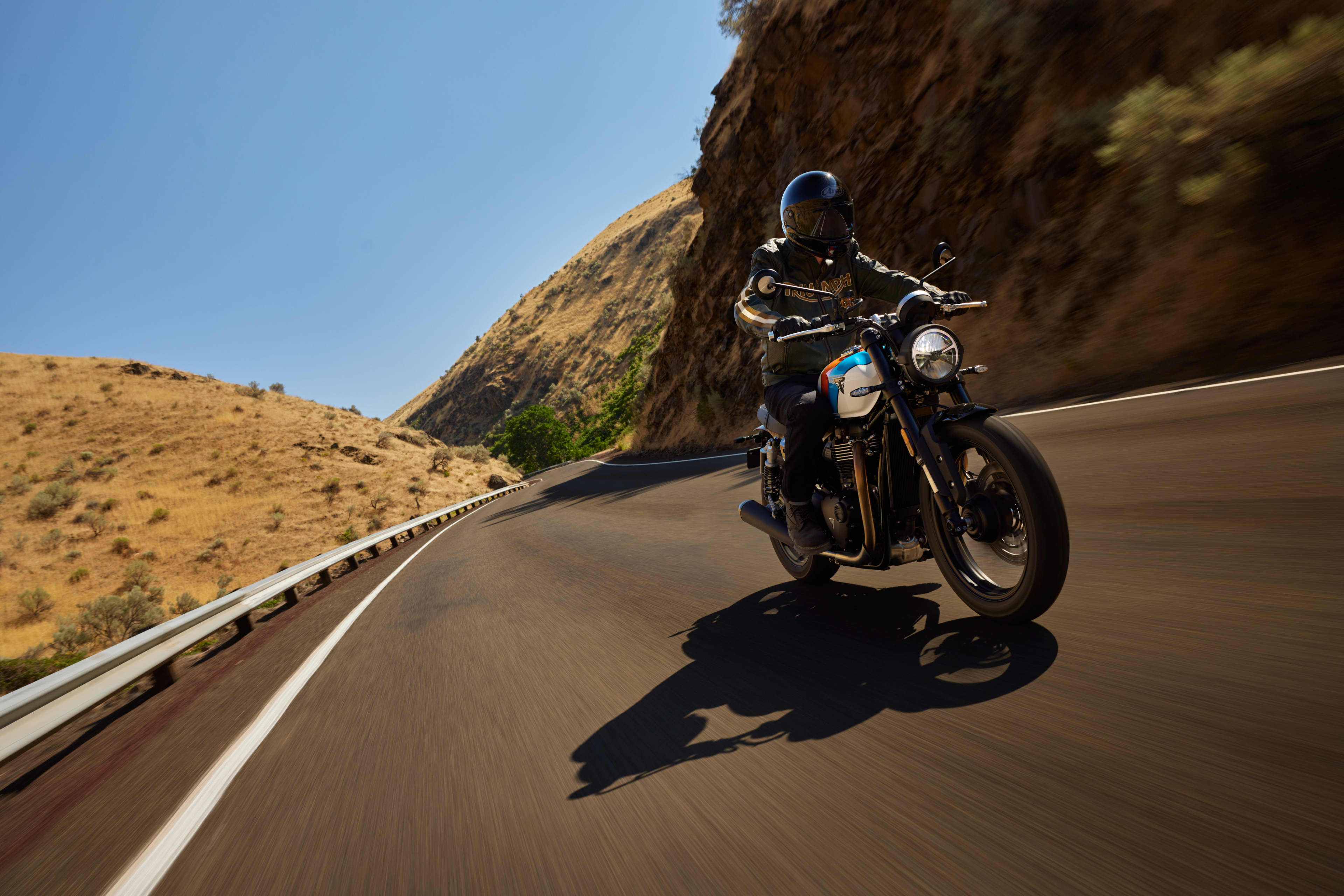 Angled right side action shot of rider on Triumph Speed Twin 900 on a road between hills