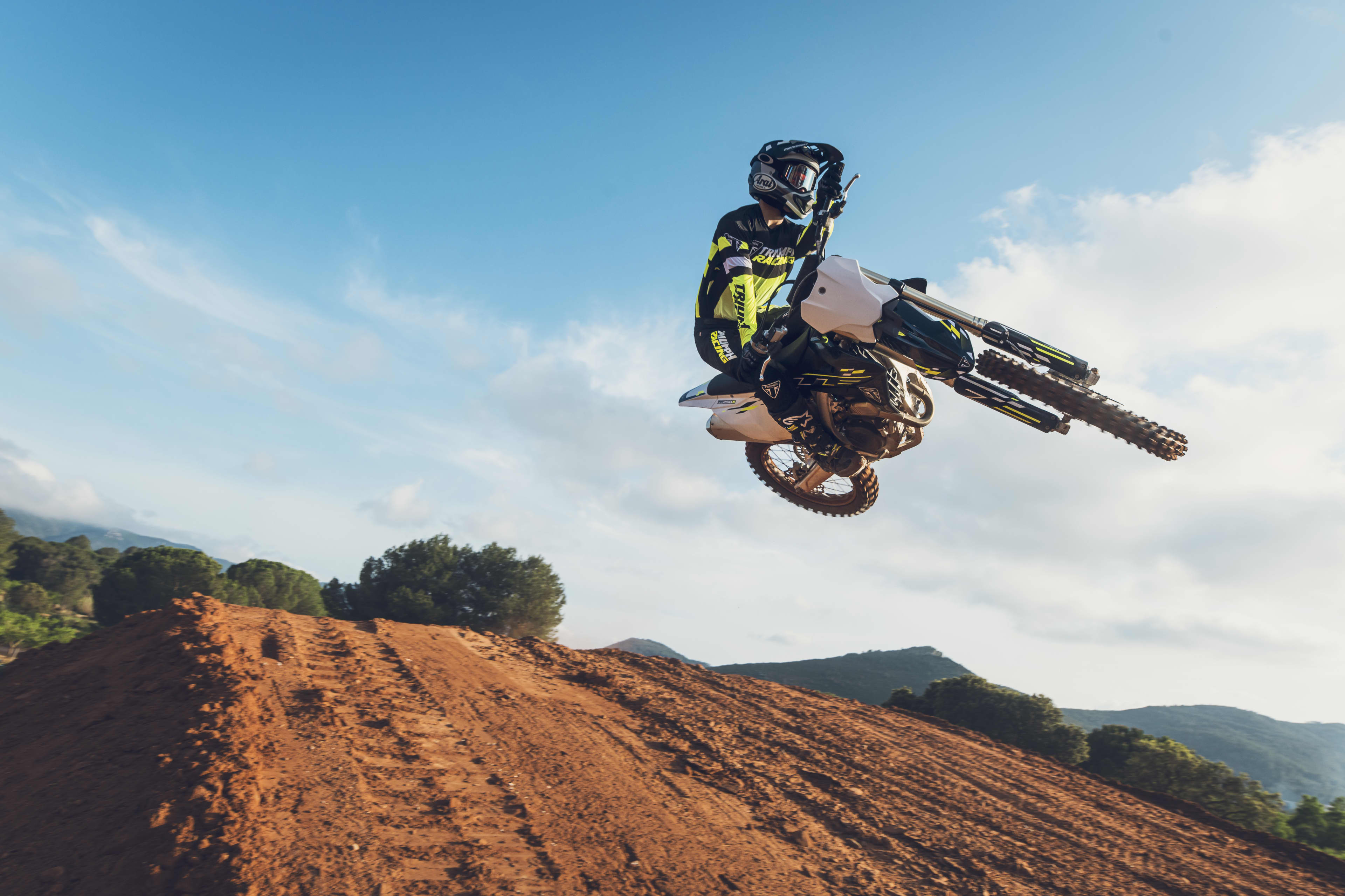 Triumph TF 250-X (MY26) with rider airborne on a motocross backdrop with blue skies