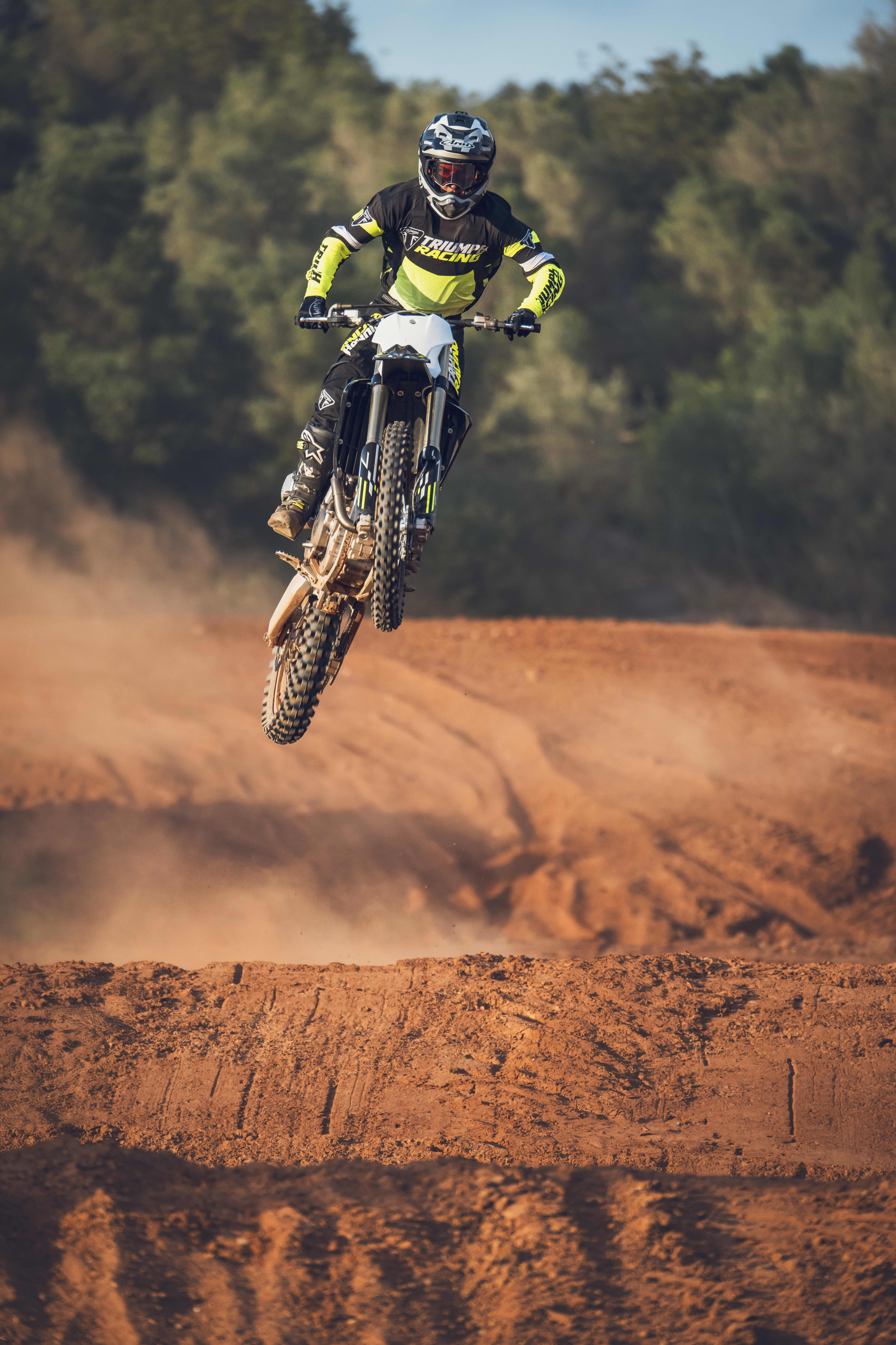 Triumph TF 250-X (MY26) airborne above a red dirt motocross landscape