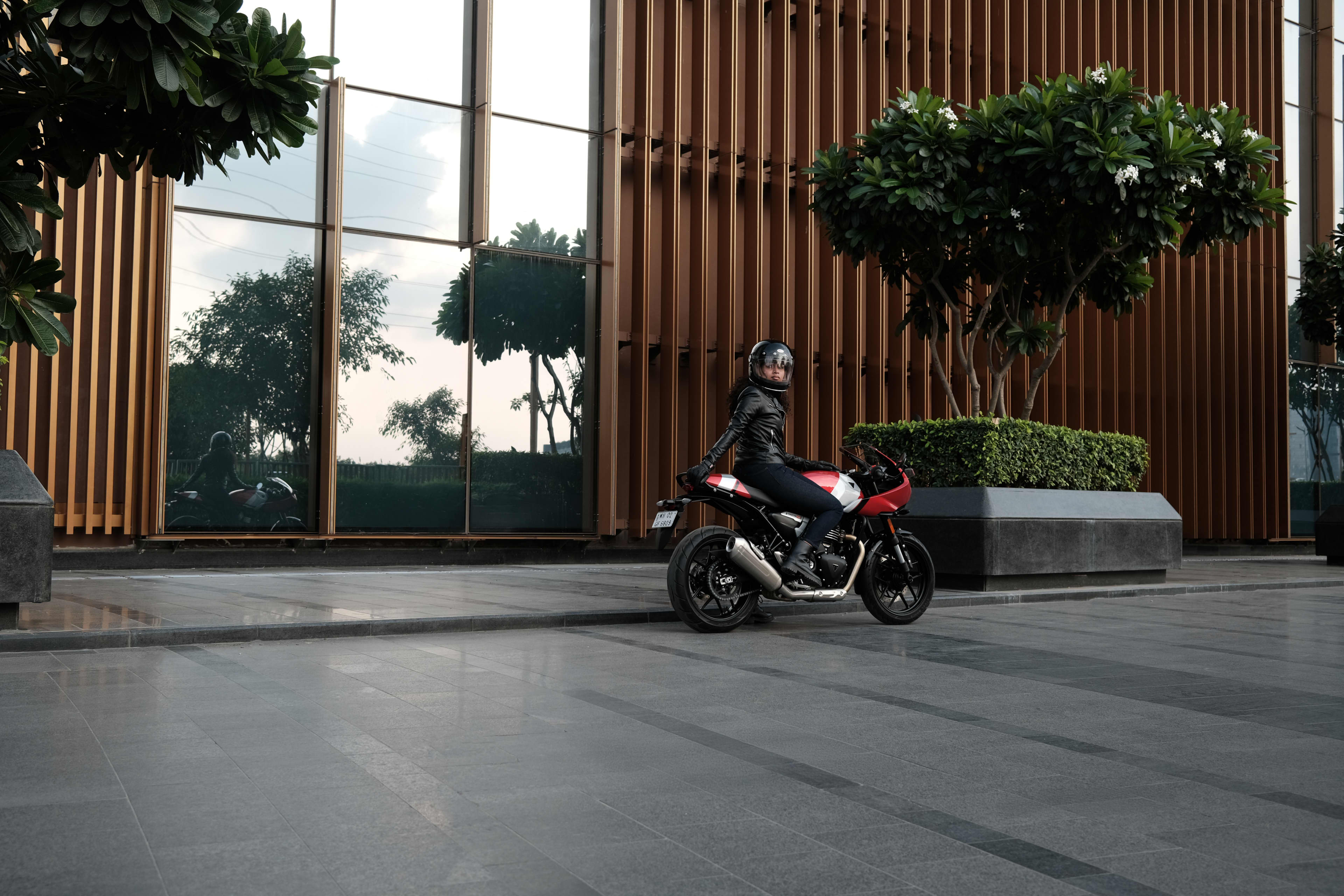 Rider sitting on a PLava red gloss and Aluminium silver Thruxton 400 in front of a building