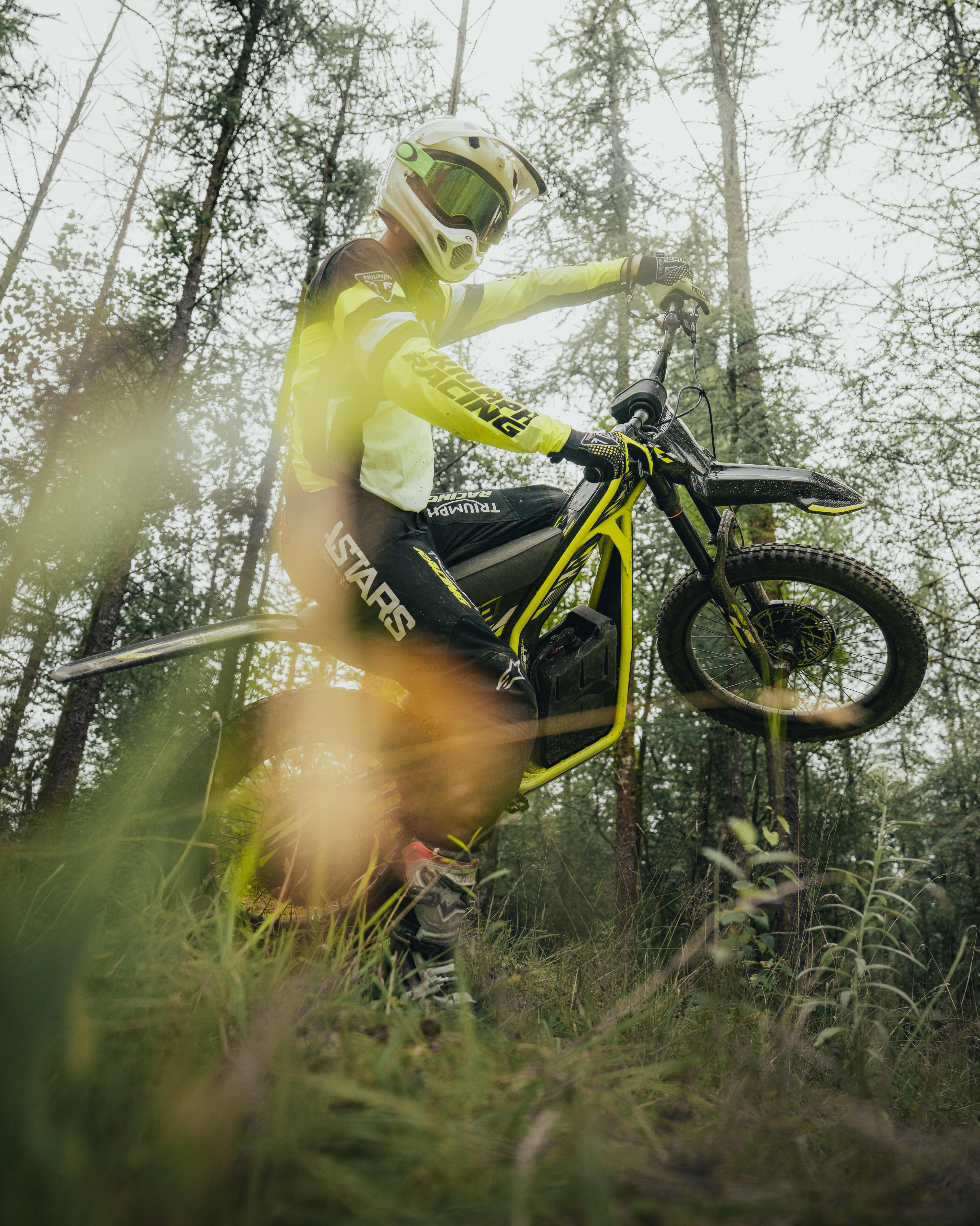 Triumph TXP-24 electric bike in air with a forest backdrop.