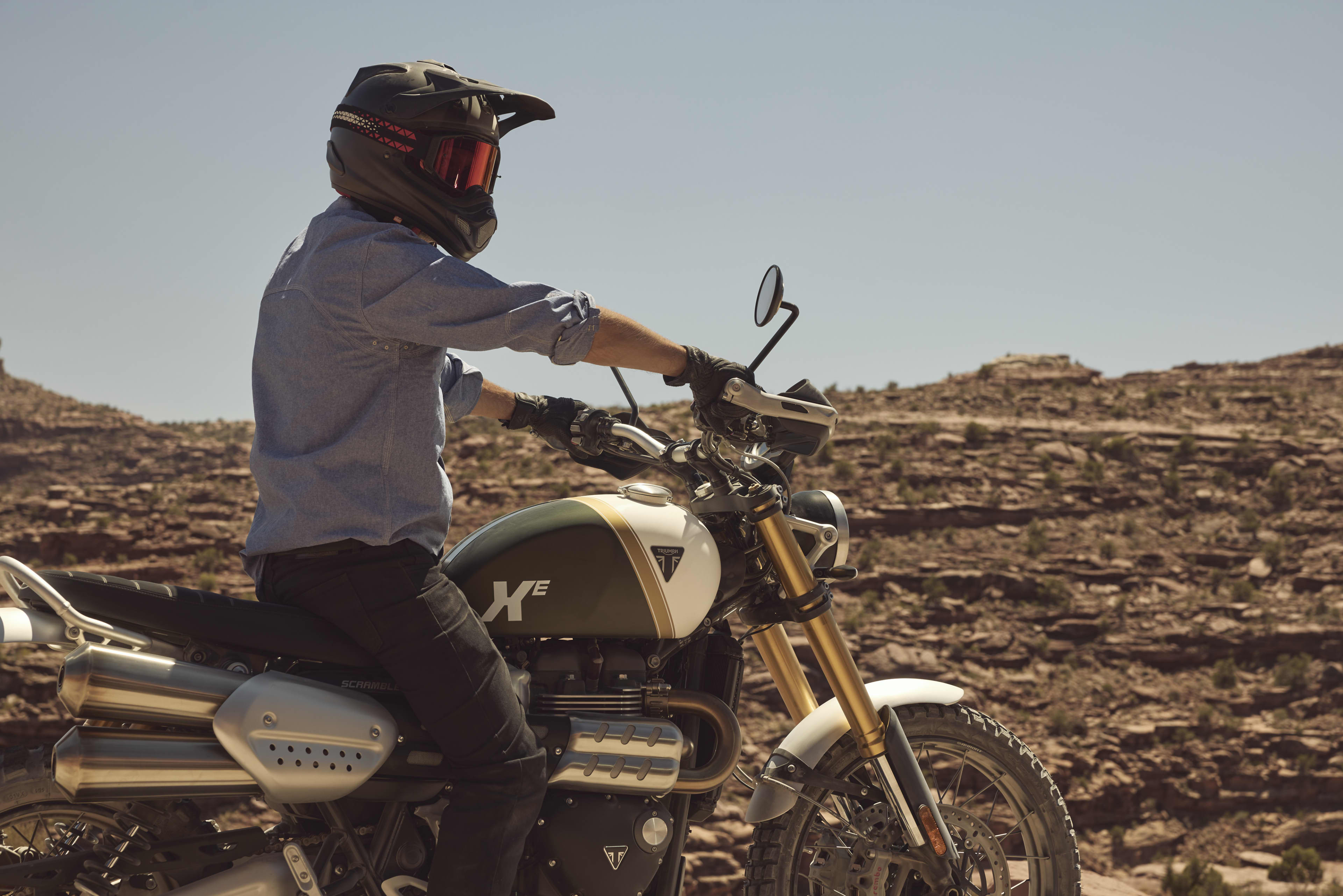 Side view of a rider sitting on a Triumph Scrambler 1200 XE surrounded by open rocky terrain