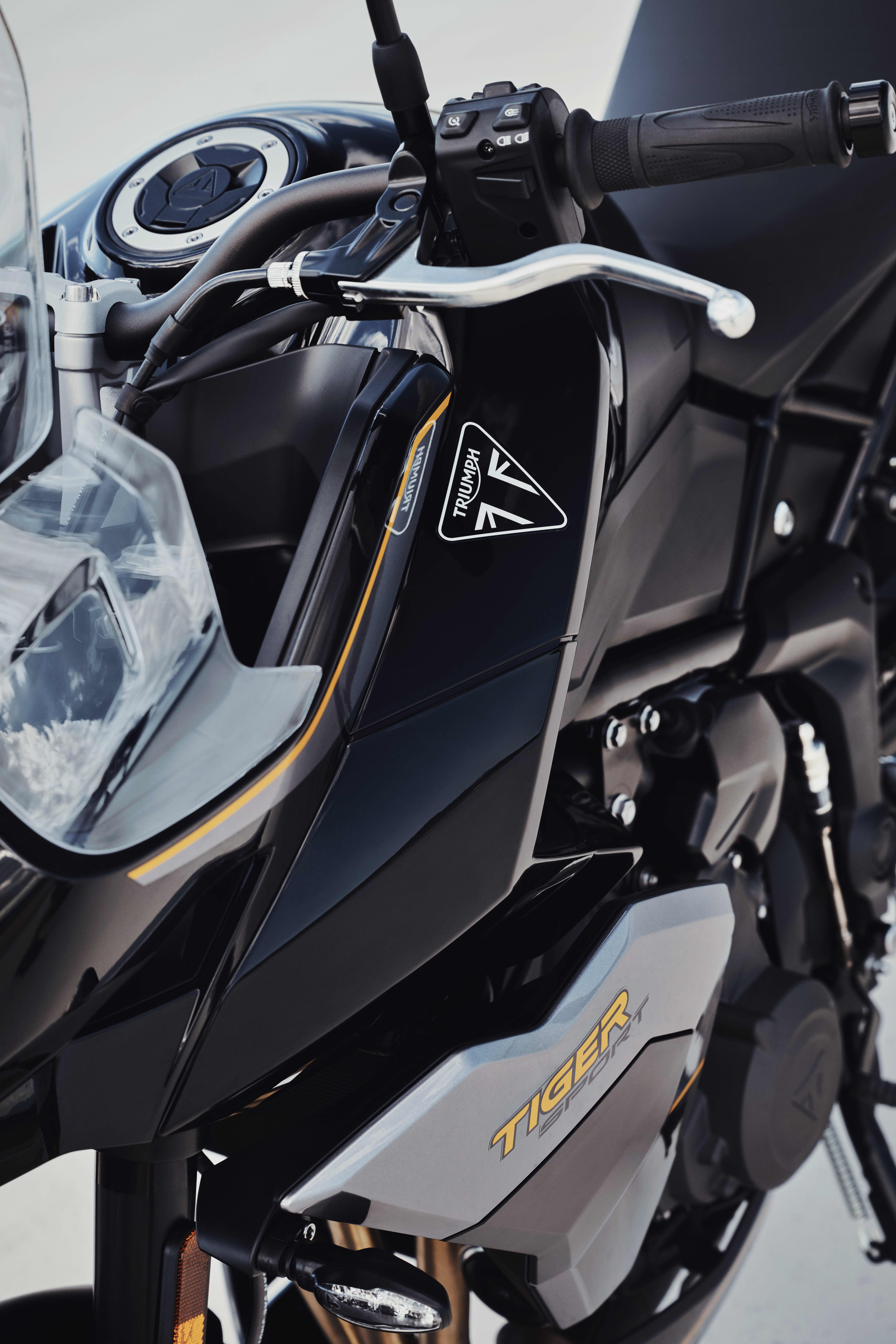 A close-up shot of the front fairing and handlebars of a black and silver Triumph Tiger Sport 800 motorcycle, highlighting the Triumph and Tiger logos.
