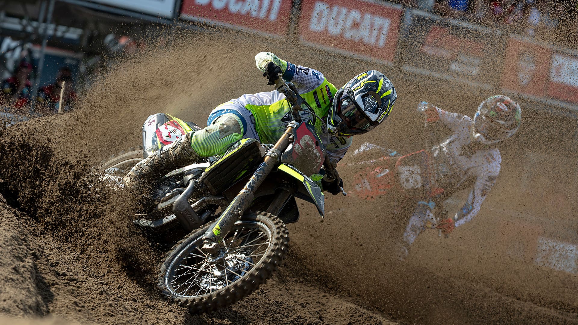 A lead Moto2 motorcycle racer leaning sharply into a turn on a racetrack, followed closely by a pack of competitors.