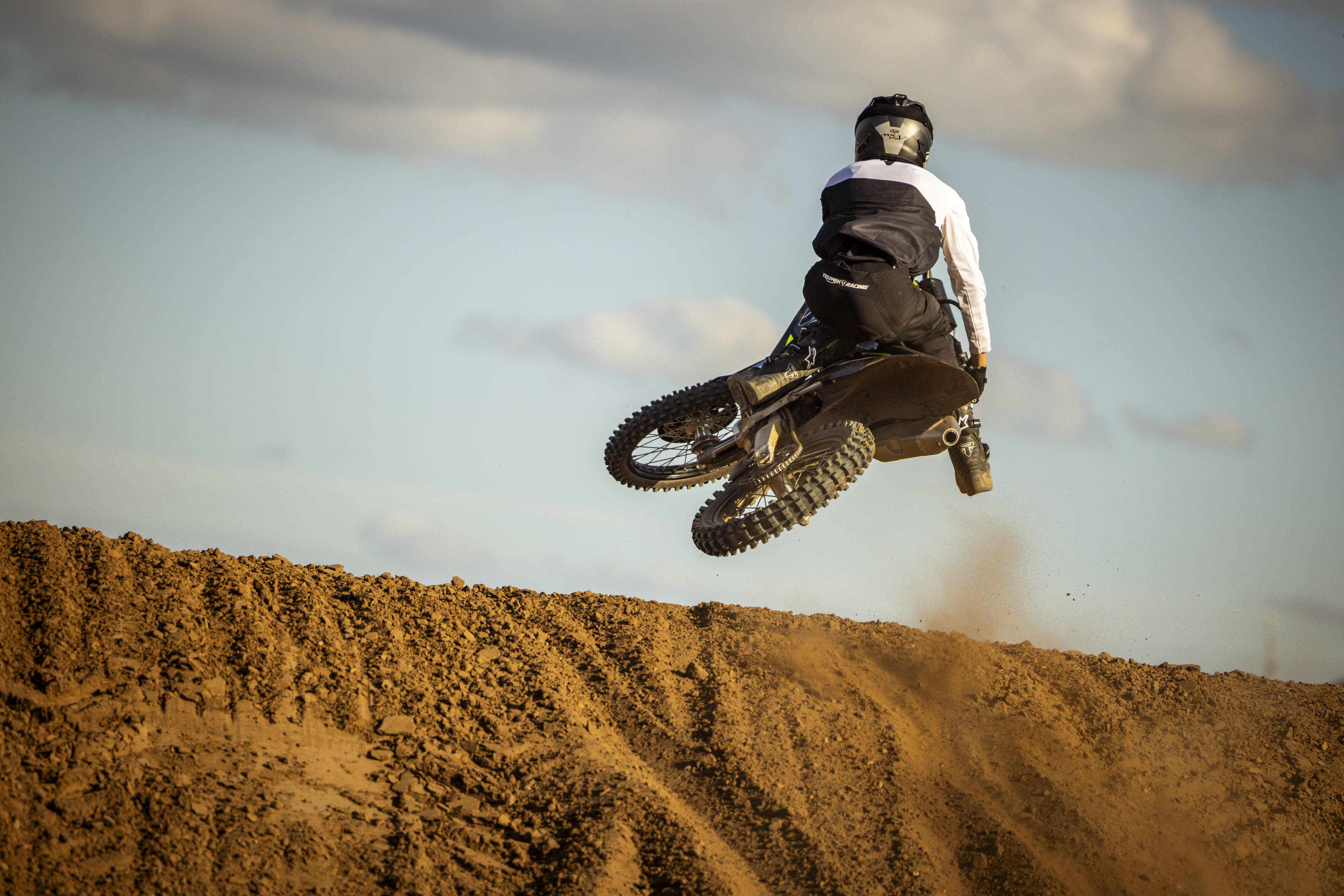 A motocross rider jumping over a dirt mound against a cloudy sky.