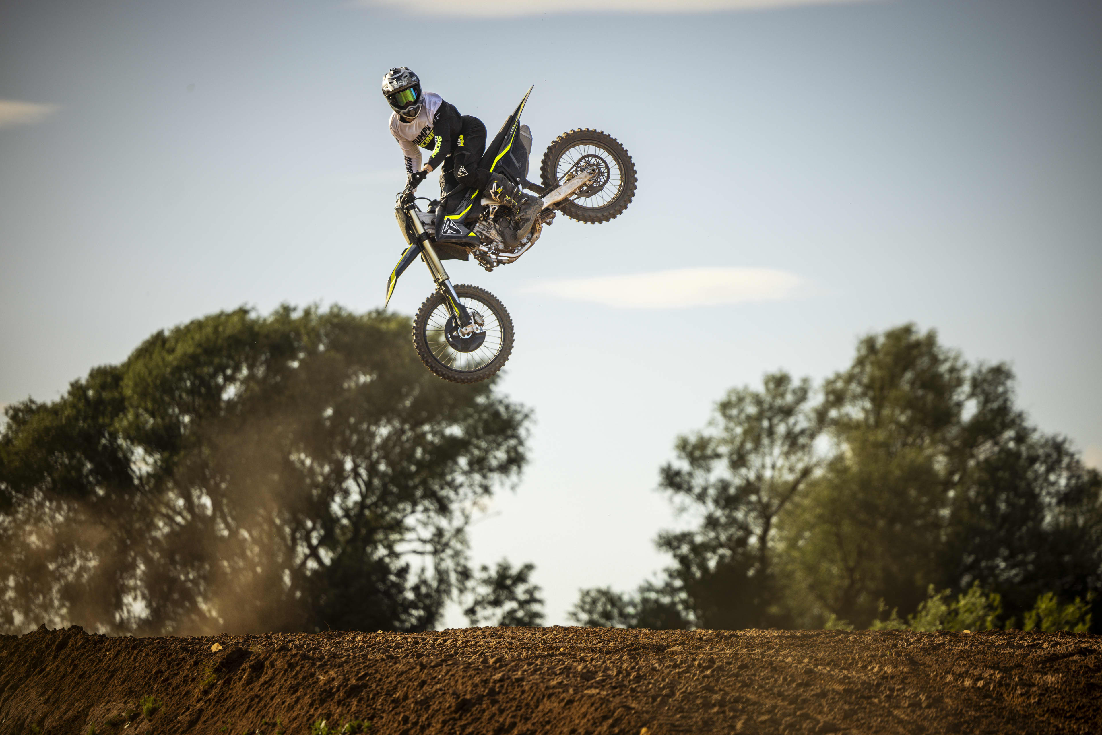 A motocross rider jumping high in the air performing a whip trick against an open sky.