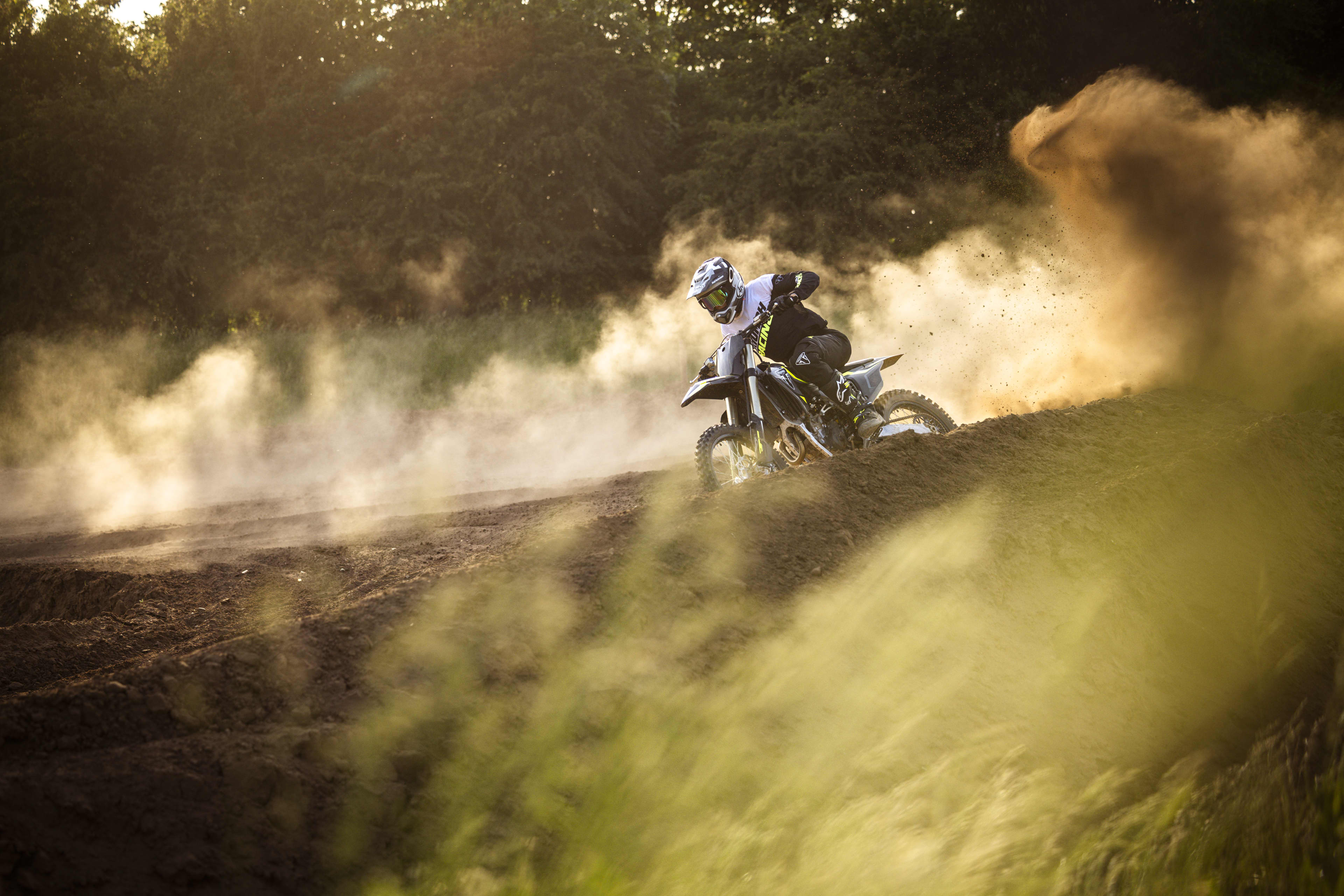A motocross rider speeding along an outdoor track surrounded by clouds of thick dust.
