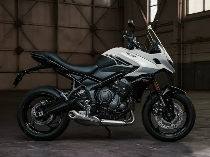 Side profile of a white and black Triumph Tiger Sport 660 motorcycle parked in an industrial hangar.