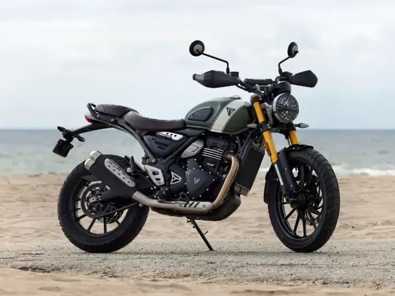A green and black scrambler-style motorcycle with gold front forks is parked beside a white wall, with its exhaust running high along the side.