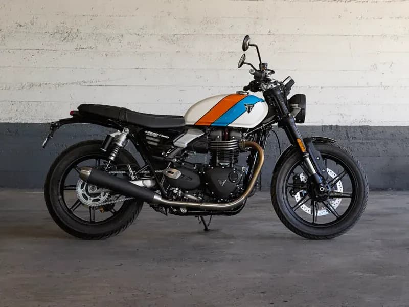 Profile view of a custom Triumph Speed 400 motorcycle featuring orange and blue fuel tank stripes in a garage.