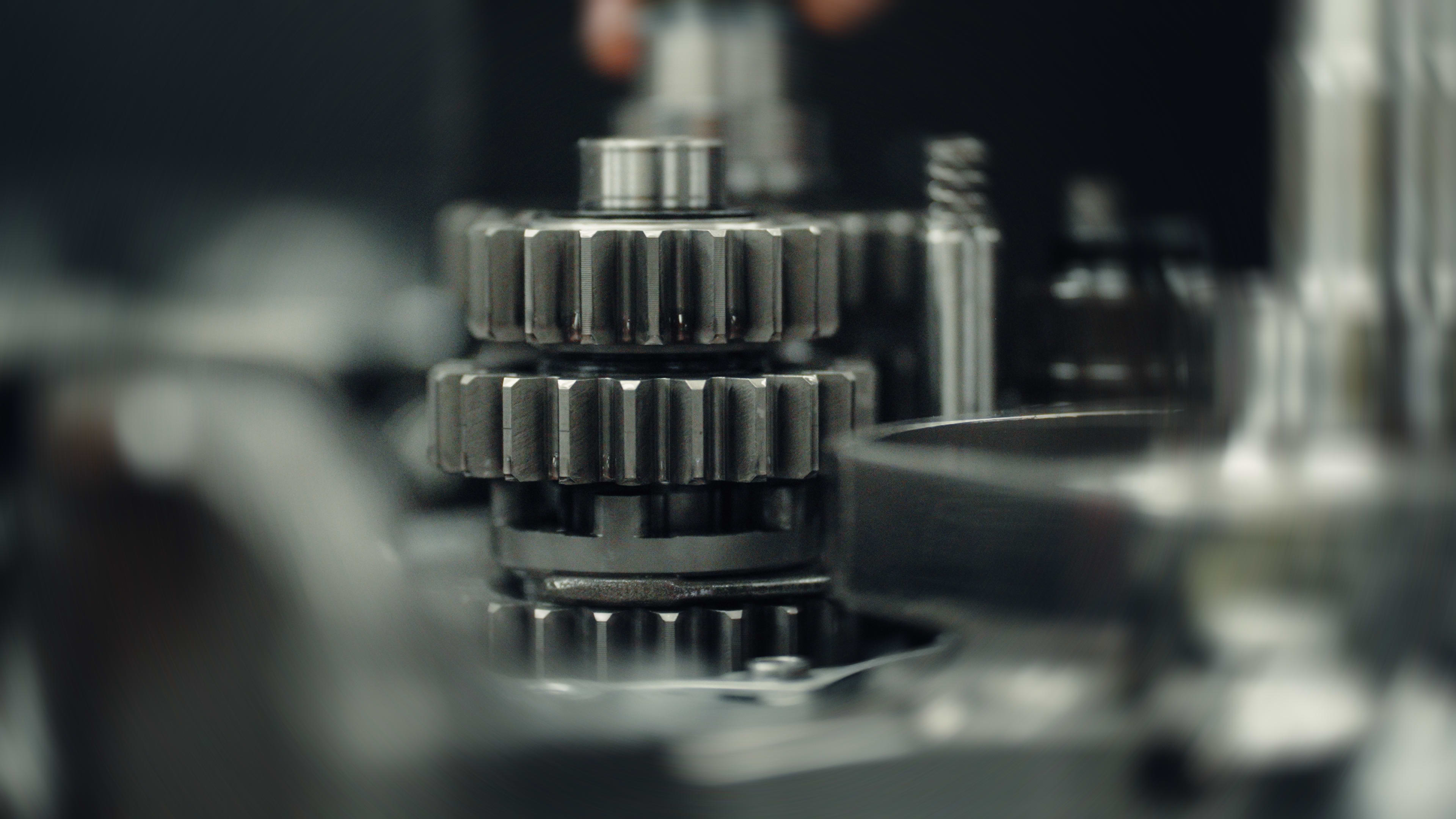 Macro shot focusing on the steel gear stack and transmission shaft assembly inside the disassembled engine case of a Triumph TF 250-X motocross motorcycle.