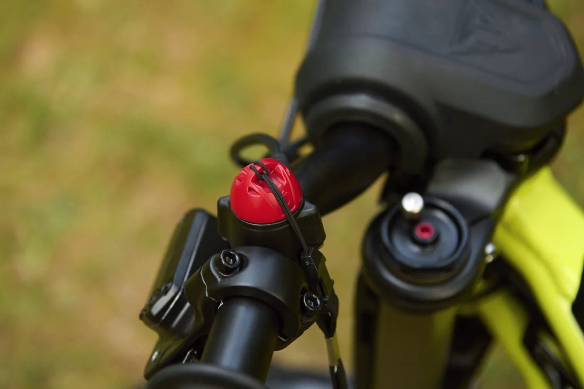Macro shot showing the red magnetic safety lanyard kill switch mounted to the handlebars next to the front fork top cap and handlebar pad on a Triumph TXP-20 youth electric motorcycle.
