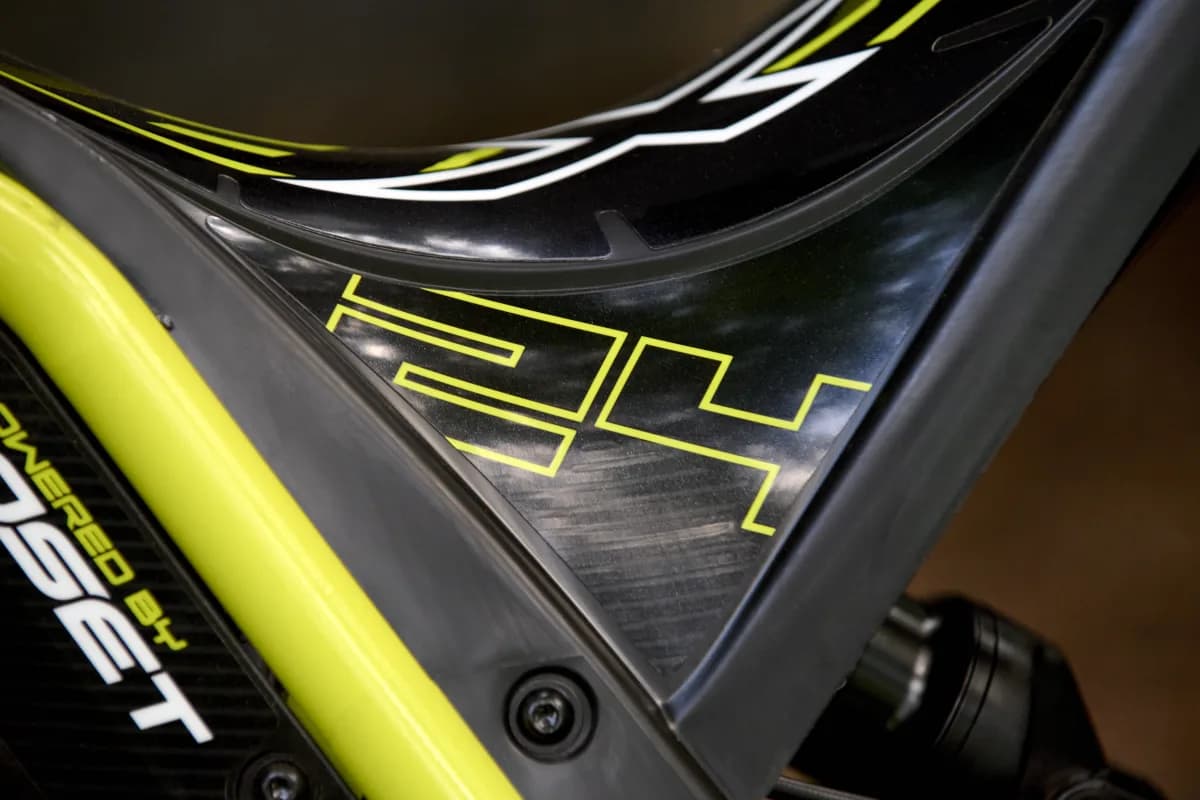 Extreme close-up detail highlighting the neon yellow '24' model outline graphic and textured panel insert on the frame of a Triumph TXP-24 youth electric motorcycle.