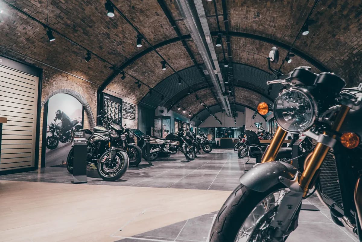 A motorcycle showroom under arched brick ceilings with several Triumph motorcycles parked along a tiled aisle.