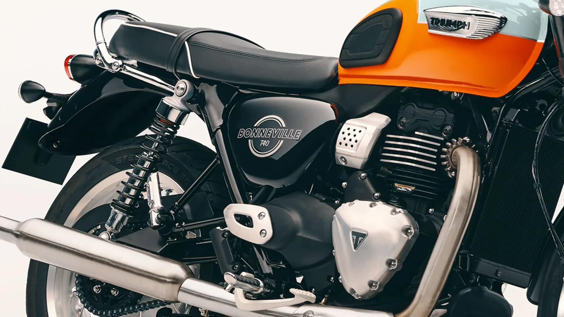 Close-up side profile showing the black bench seat, engine block, Bonneville T40 badge, and orange tank on a Triumph motorcycle.