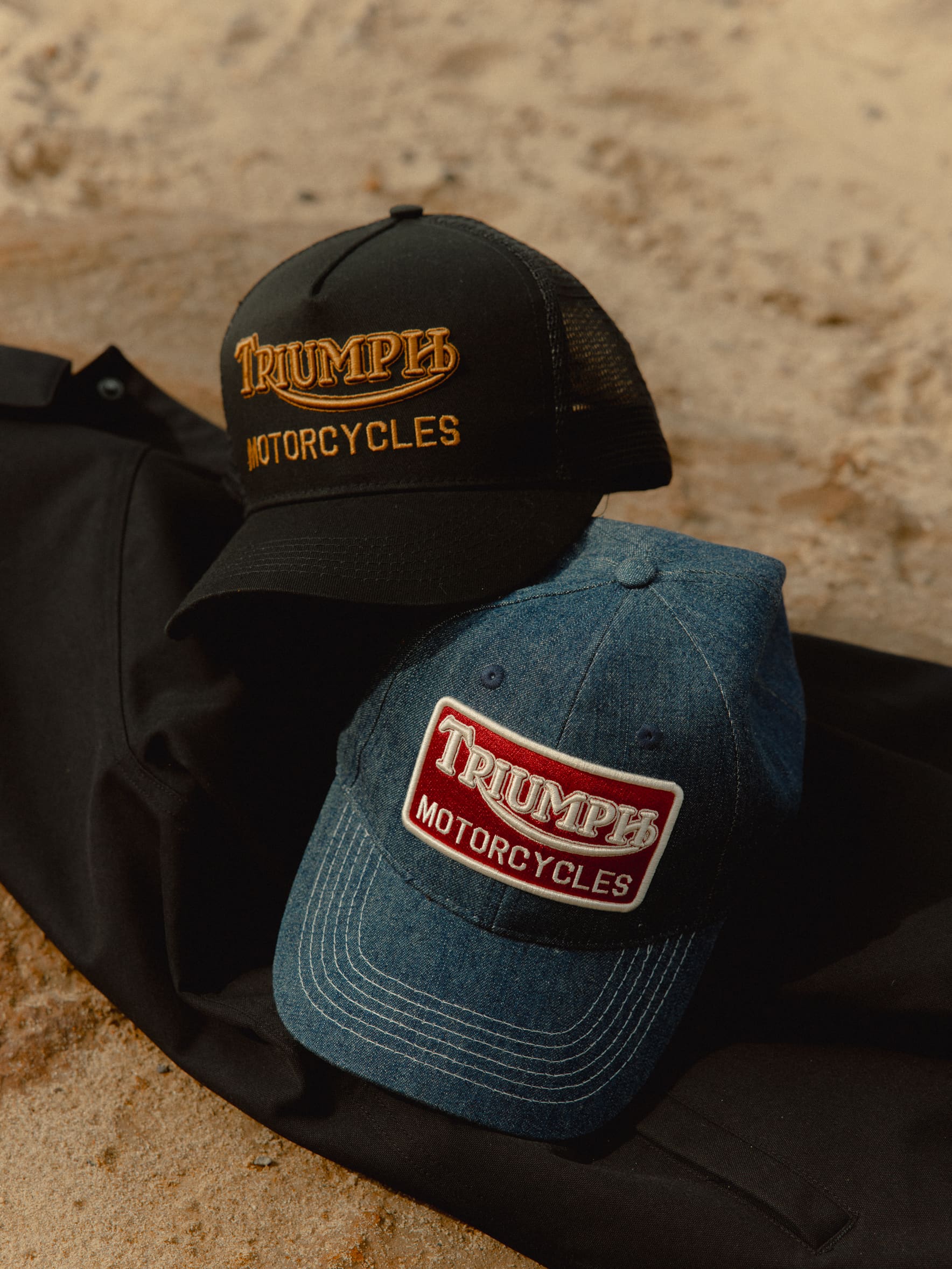 FAQs, DELIVERY & RETURNS Close up of Triumph Heritage Trucker Caps on sand