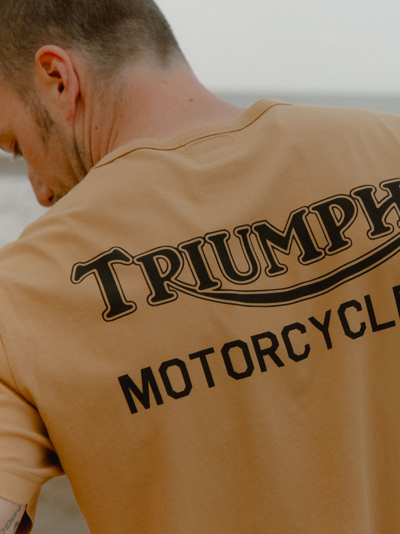 SHIPPING & DELIVERY Man wearing fawn Triumph Motorcycles Heritage Adcote Back Print Tee