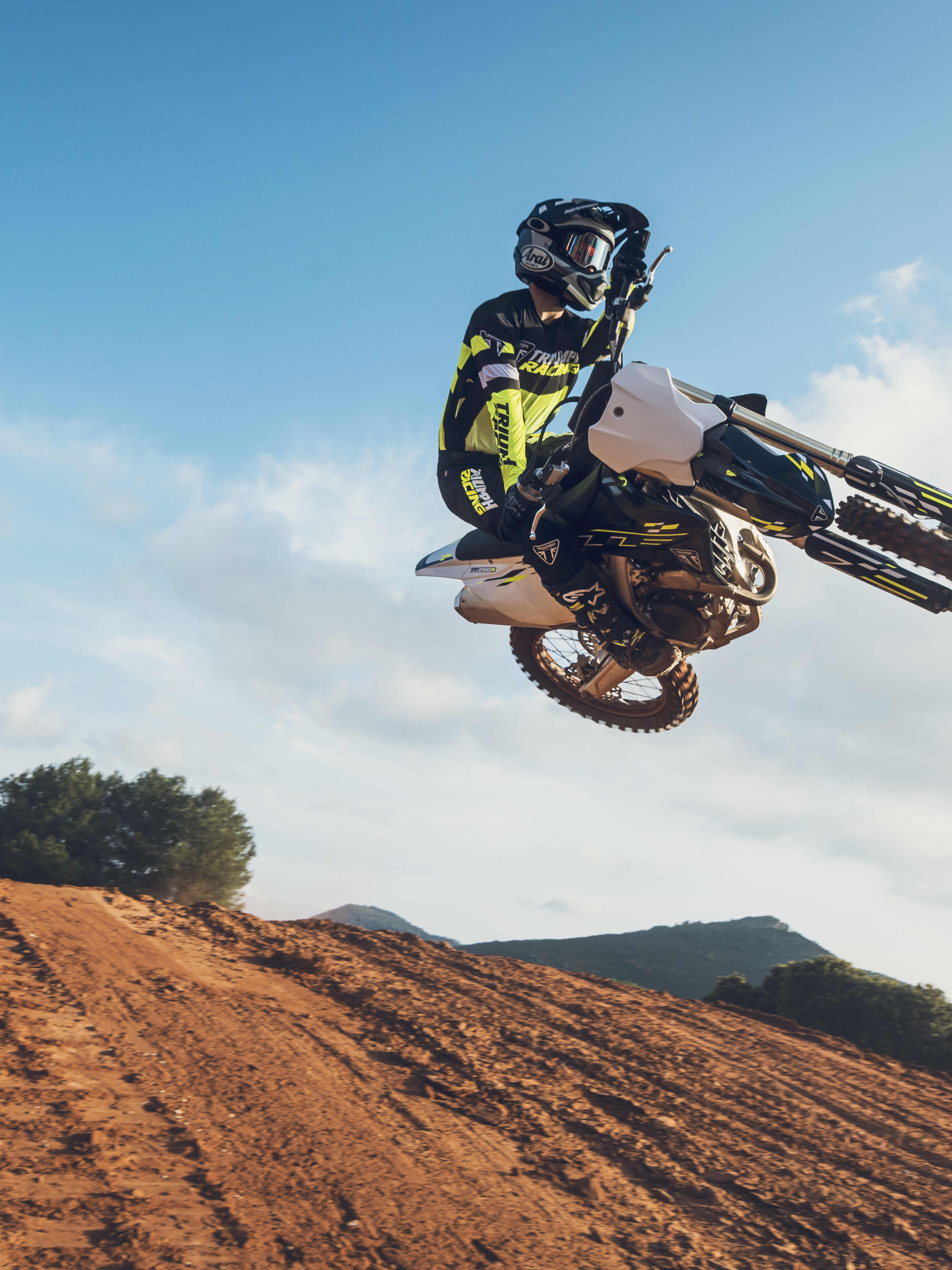 A motocross rider leaning heavily into a turn on a Triumph 250-X motocross bike, kicking up a large cloud of dust.