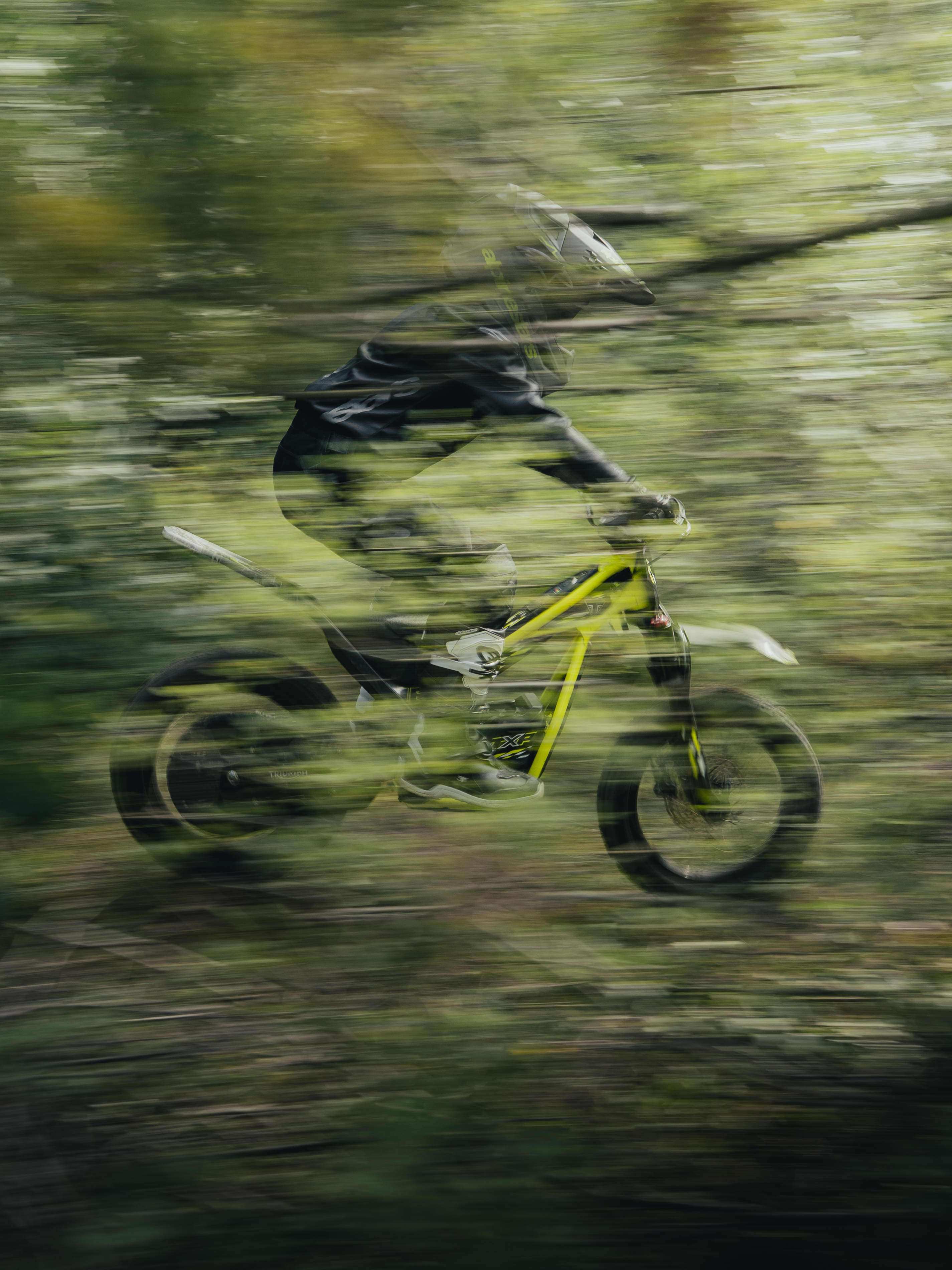 Triumph TXP with young rider through a forest.