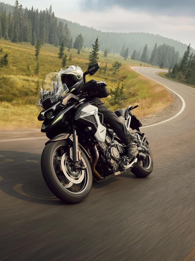 Nouvelle Tiger 1200 GT Pro Action photo of a Triumph Tiger 1200 GT Pro adventure motorcycle leaning into a curve on a scenic mountain highway.