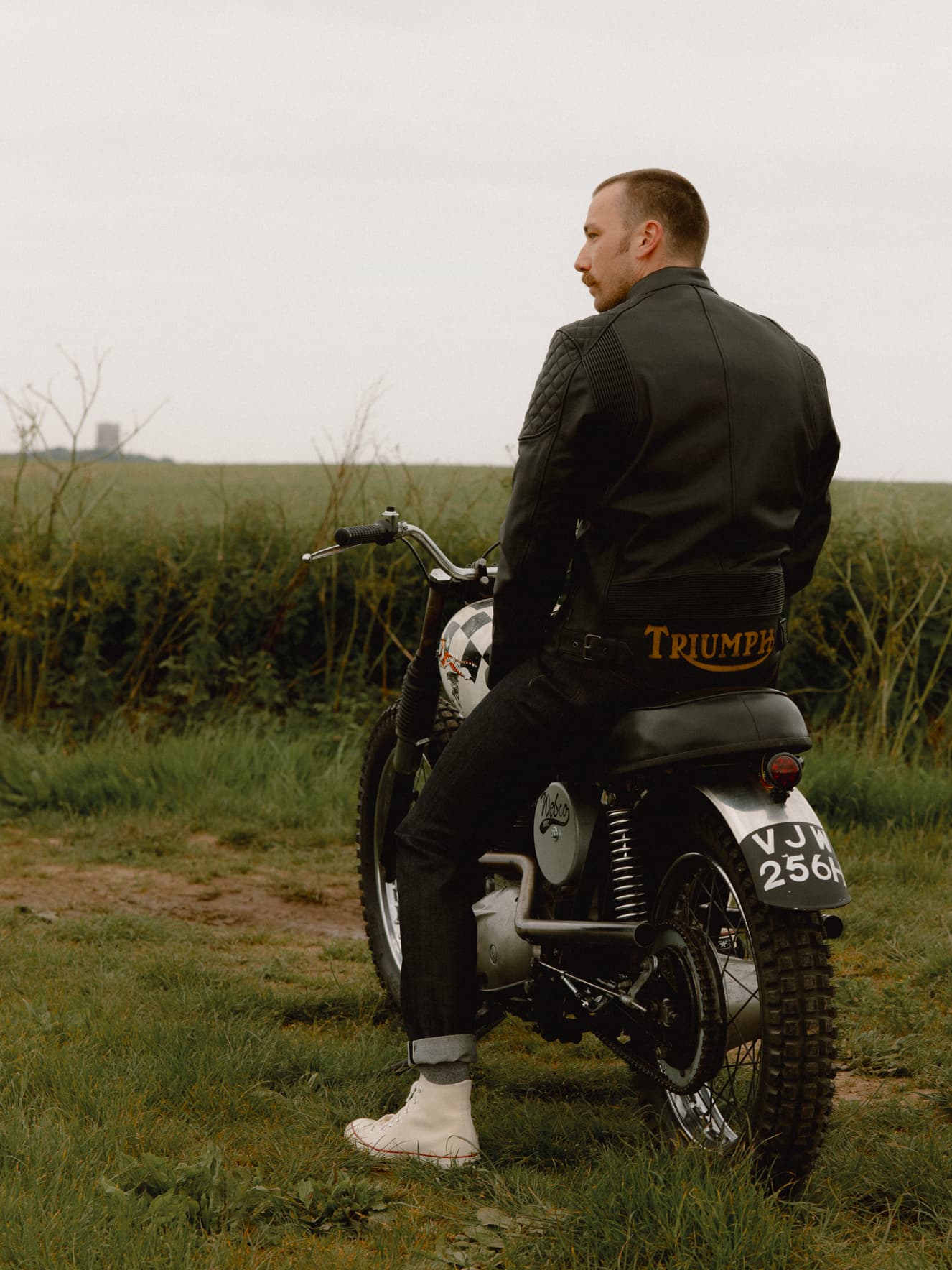 Man sitting on bike in a field with a leather jacket on