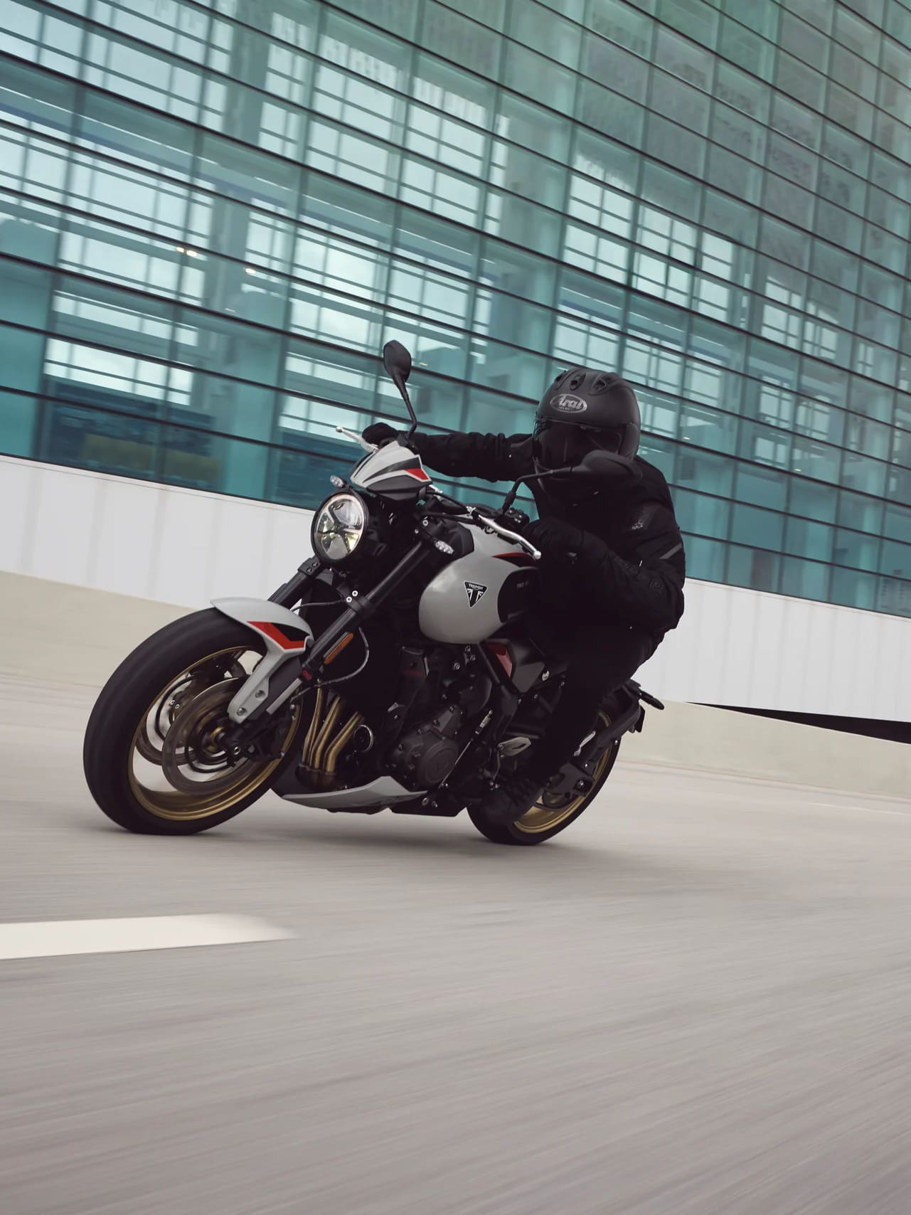 Rider on a Triumph Trident 800 beside a modern glass-fronted building.