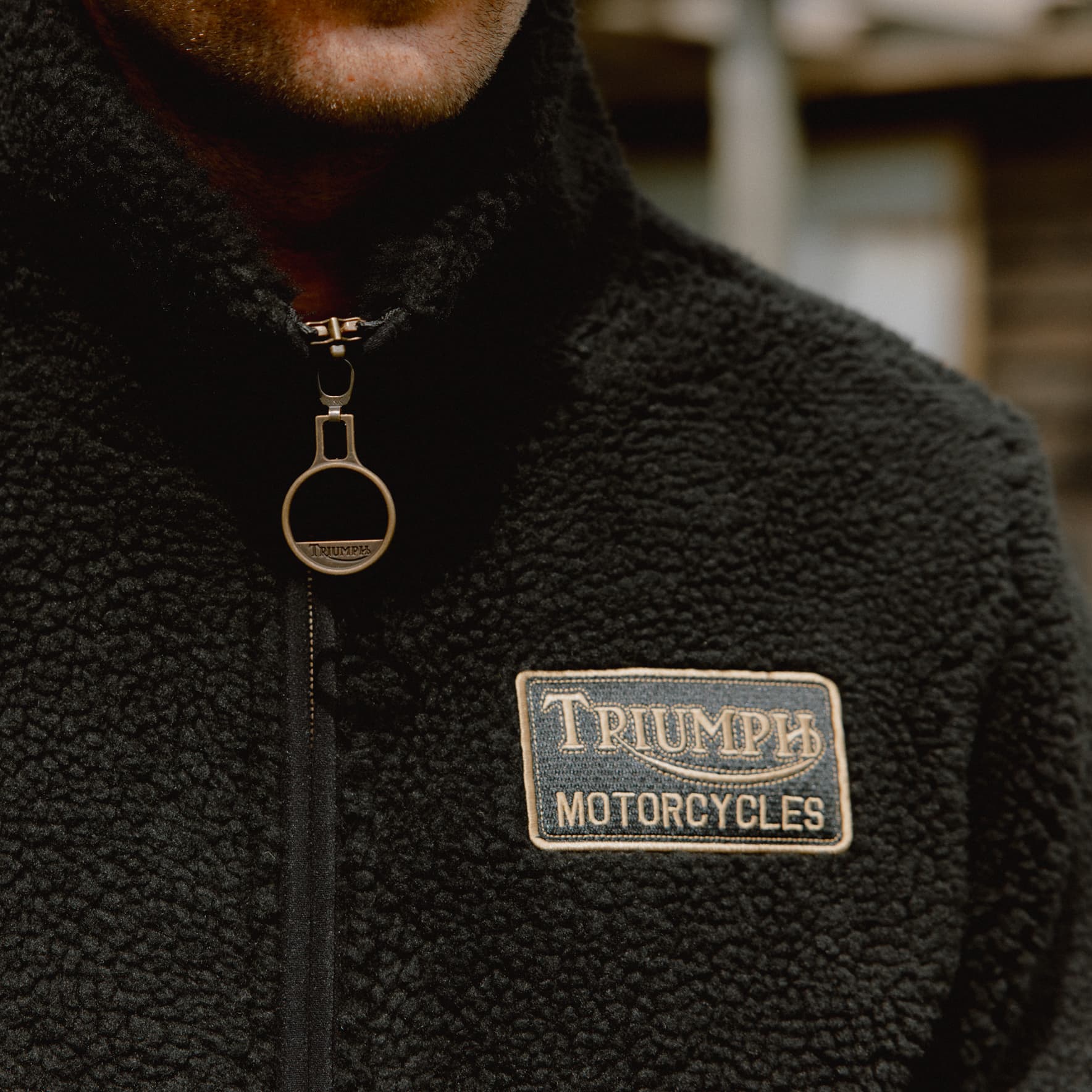 TERMS AND CONDITIONS Close up of man wearing a Roadhouse High-Pile Fleece with Triumph Motorcycles badge in gold
