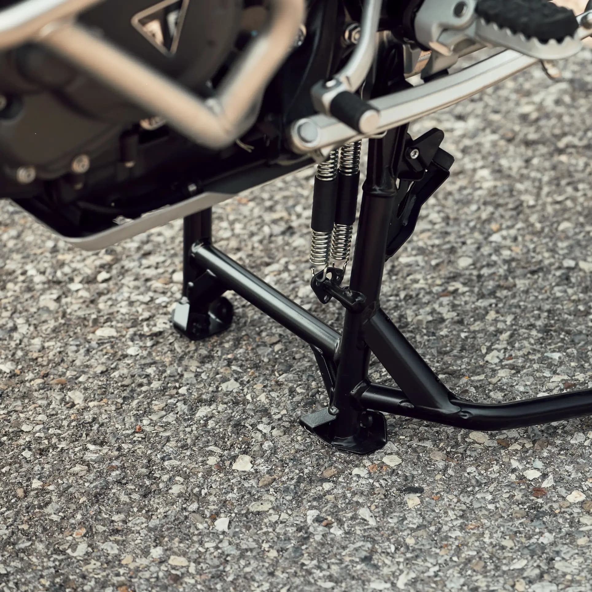 La géométrie optimisée de la béquille associée à la commande de suspension automatique facilite considérablement le levage de la moto sur la béquille centrale. Lorsque la béquille centrale est déployée, la suspension se met sous pression pour réduire l’affaissement et relever l’arrière de la moto, pour une manipulation plus simple et mieux maîtrisée, même lorsque la Tiger 1200 est complètement chargée. Lors de l’utilisation de la béquille latérale, la précharge arrière est automatiquement réduite à son réglage minimum ; la moto s’abaisse alors au maximum, ce qui permet de replier la béquille sans effort au moment de remonter en selle et de repartir.