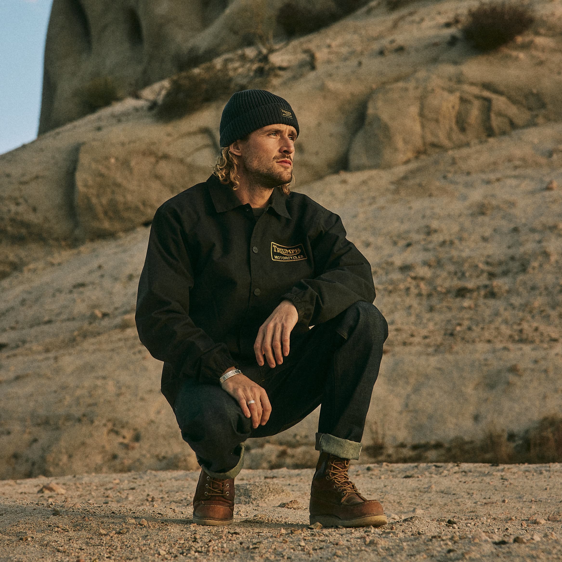 Man kneeling down while wearing Triumph Motorcycle Oiley Jacket and Cap