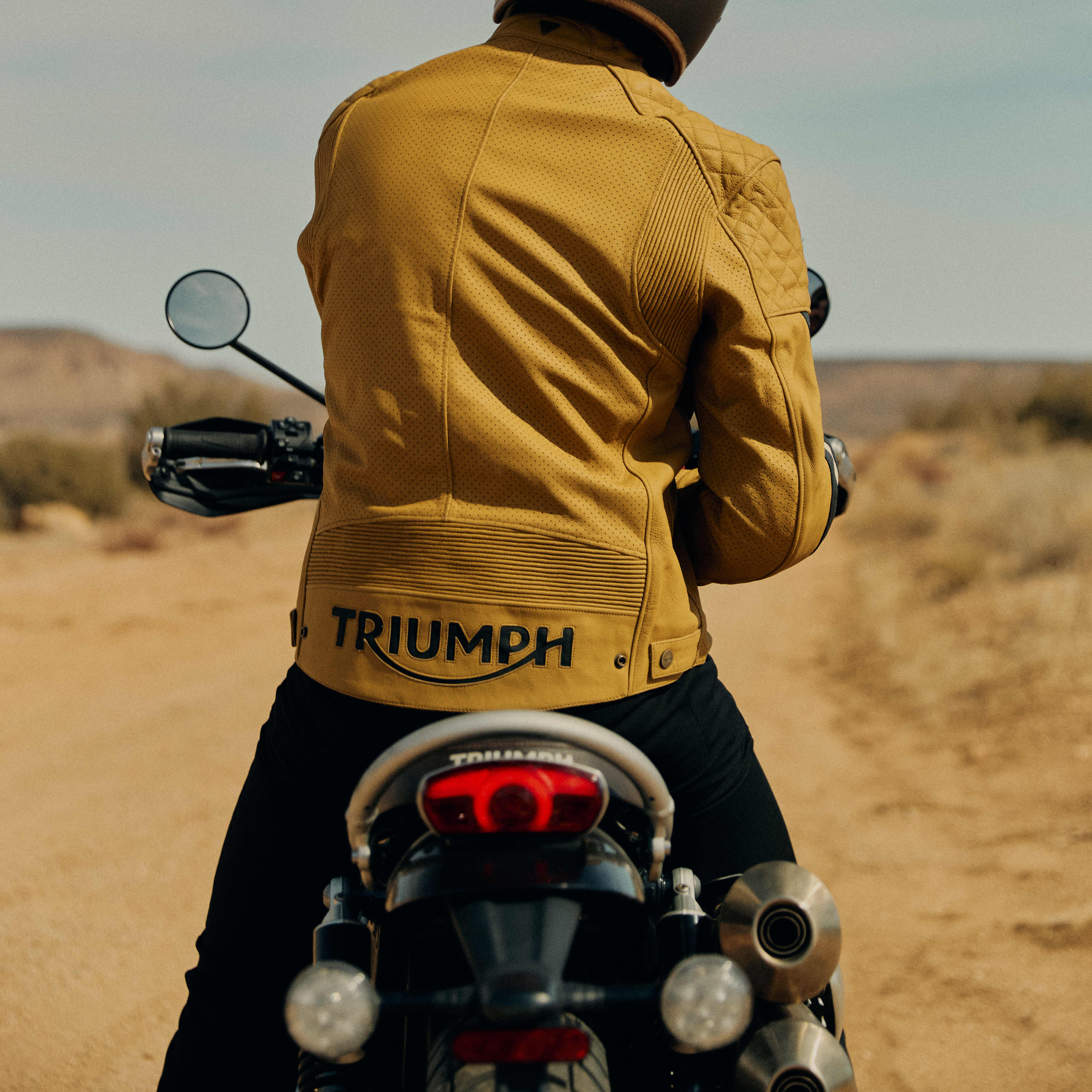 Mans back on a Triumph Motorcycle while wearing a yellow Triumph Braddan Jacket