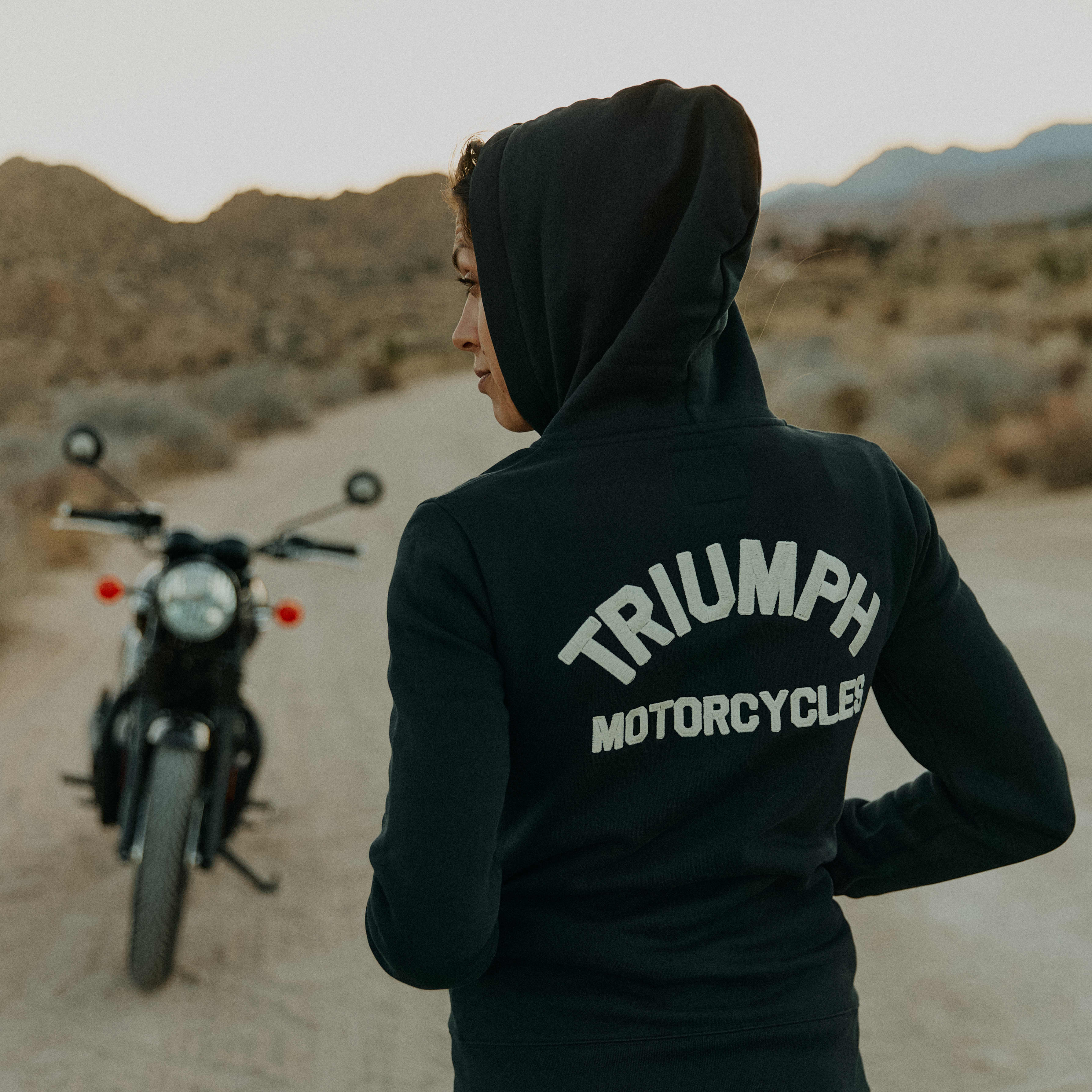 Women in desert with a motorcycle in a desert wearing a black Triumph Motorcycles hoodie