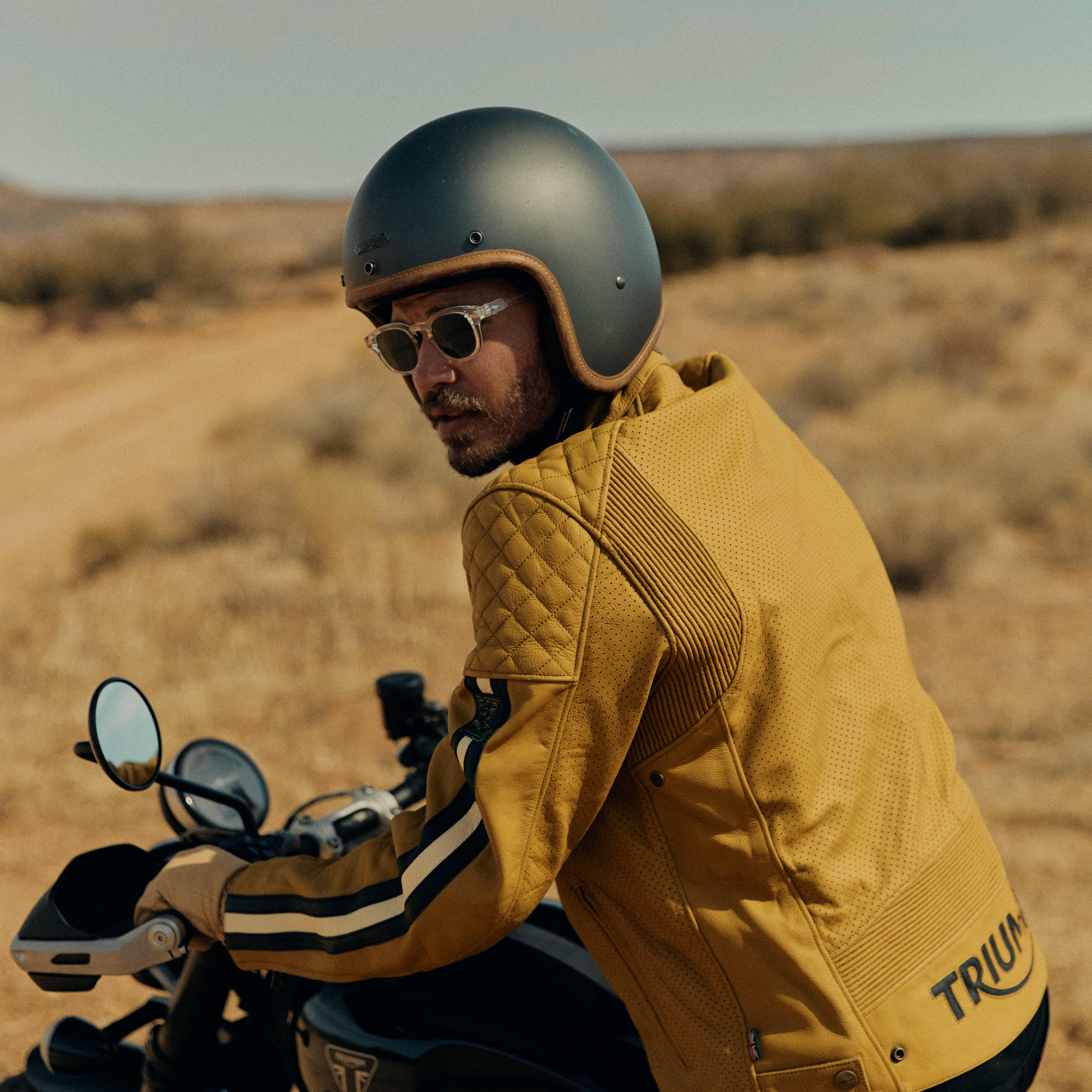 Man on a bike in the desert wearing a yellow Triumph motorcycle jacket