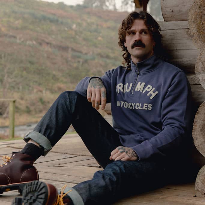 Man sitting down wearing a blue Triumph Motorcycles Quarter Zip Sweat
