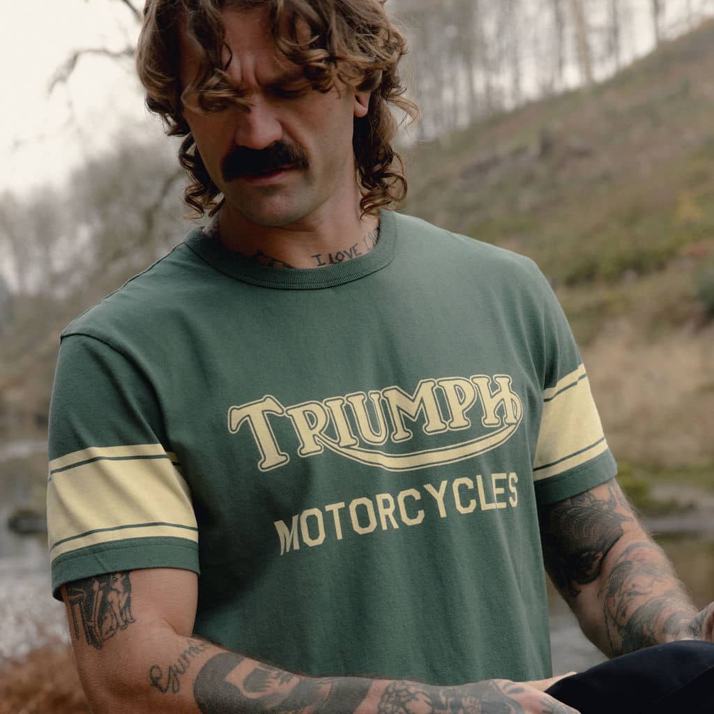 Man taking off jacket wearing a green Triumph Motorcycles T-shirt