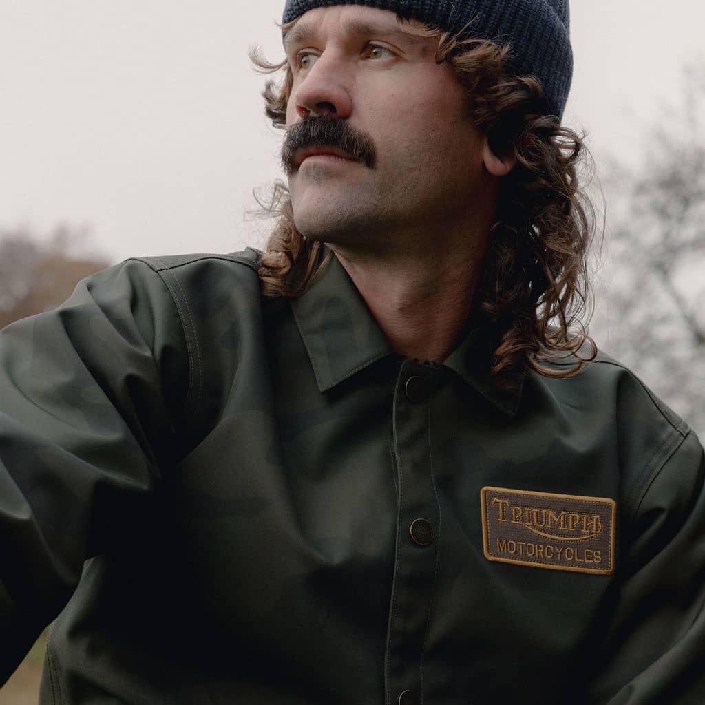 Man looking in the distance wearing a camo Triumph Heritage Jacket