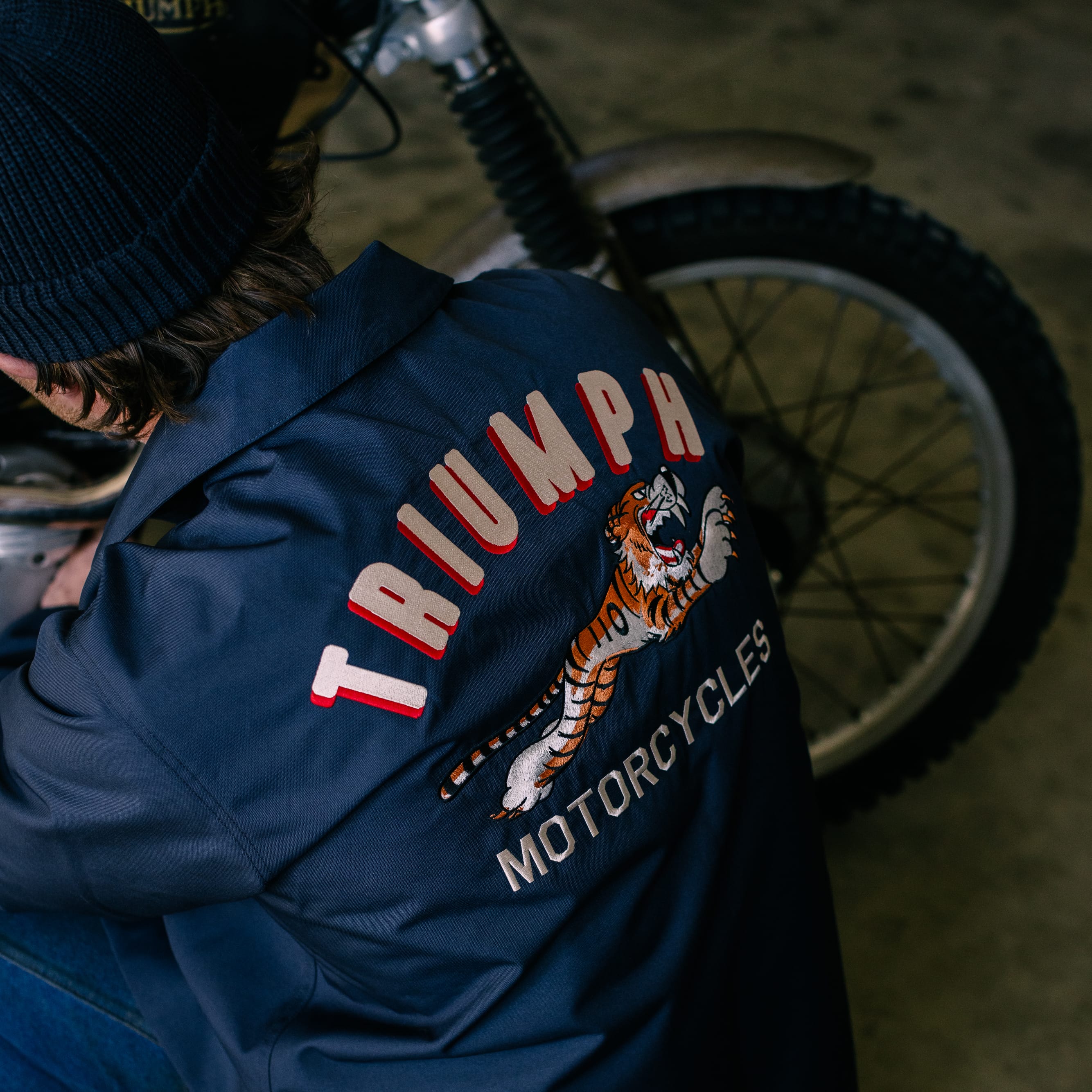Man looking at a motorbike in a garage while wearing a Triumph Heritage jacket