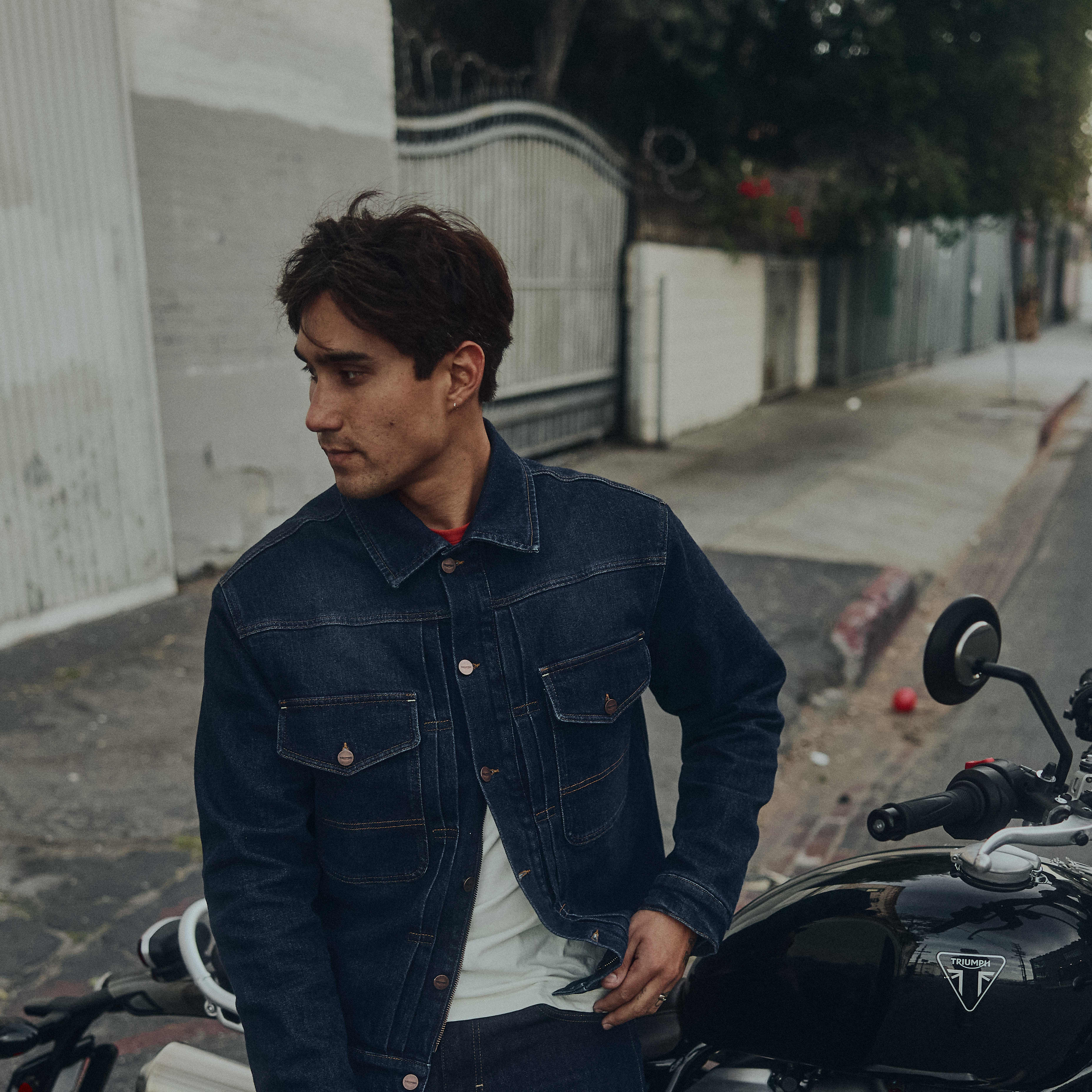 Man leaning against a Triumph Motorcycle wearing Jax Denim Riding Jacket