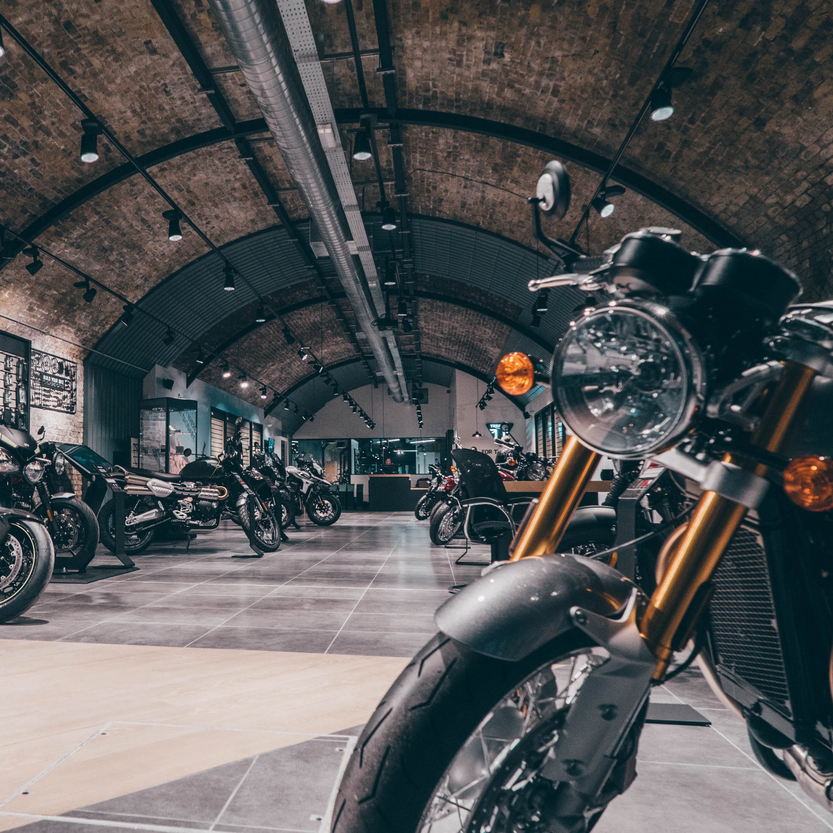 A motorcycle showroom under arched brick ceilings with several Triumph motorcycles parked along a tiled aisle.
