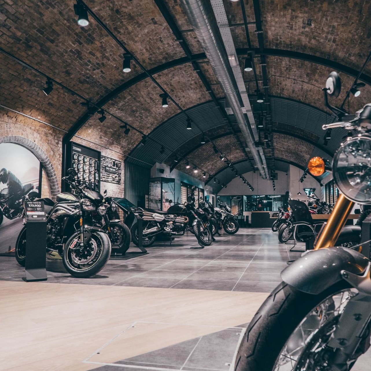 A motorcycle showroom under arched brick ceilings with several Triumph motorcycles parked along a tiled aisle.