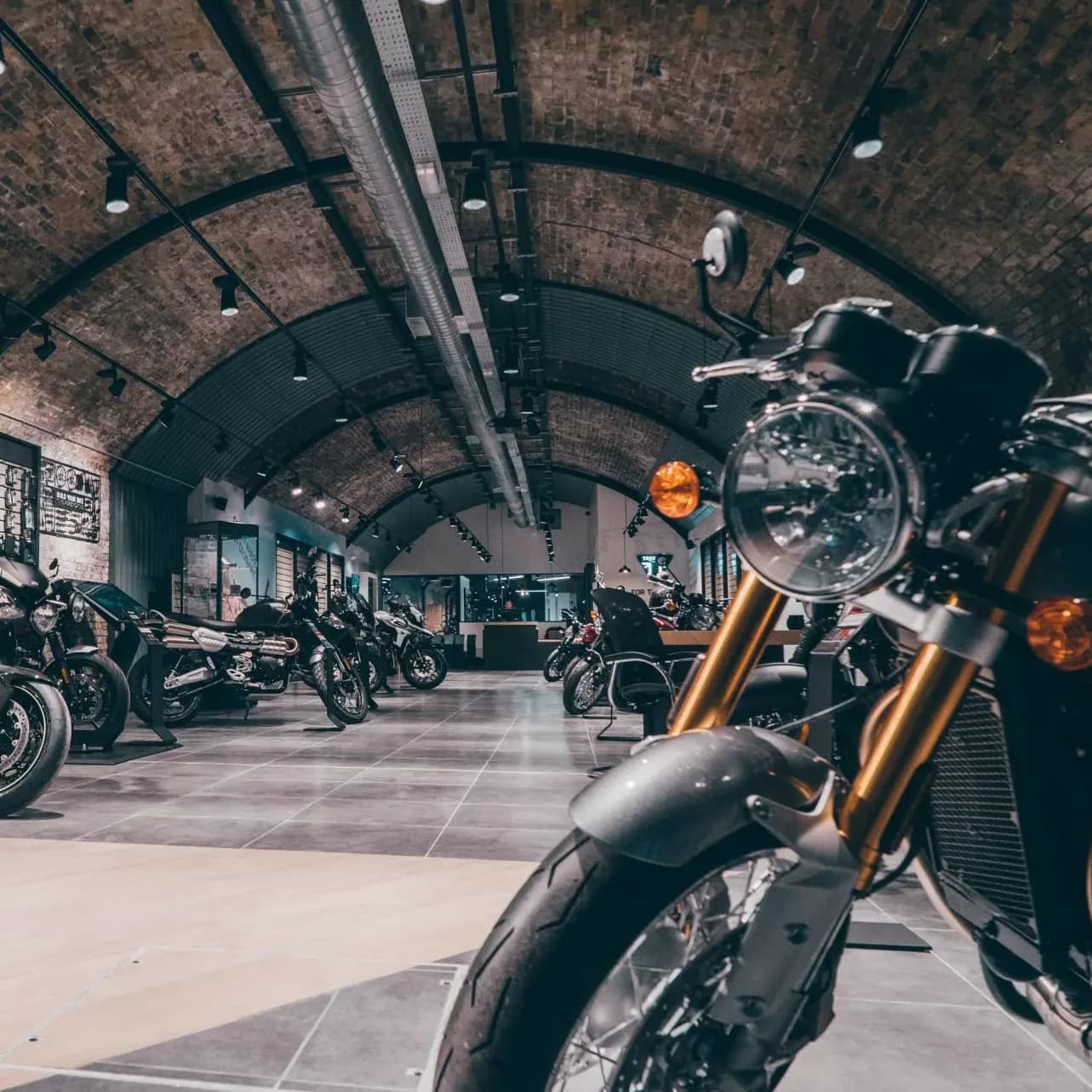 A motorcycle showroom under arched brick ceilings with several Triumph motorcycles parked along a tiled aisle.